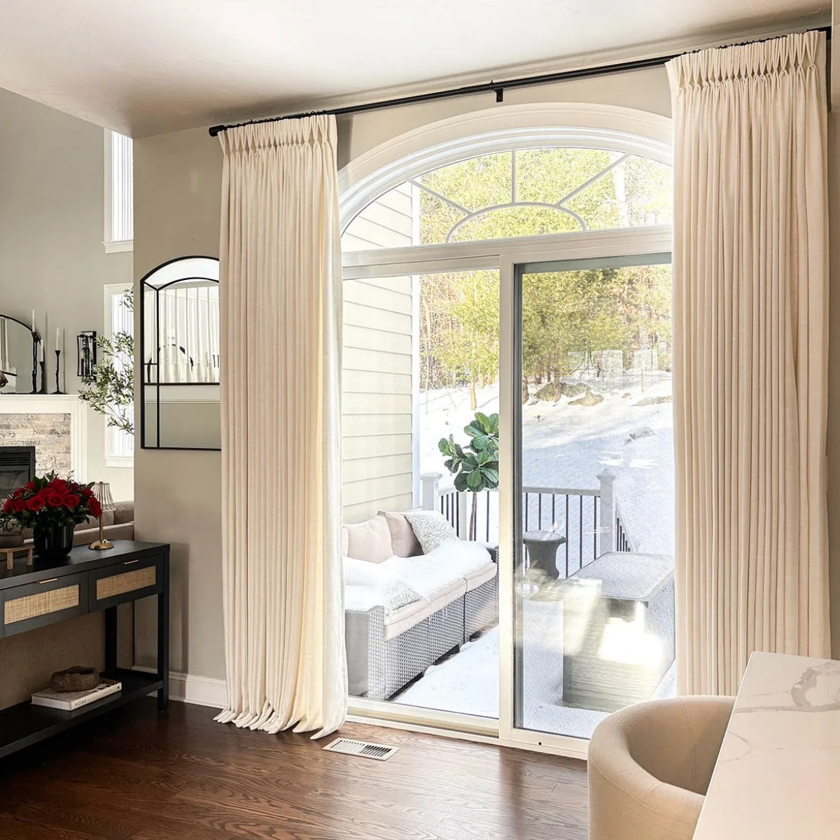Two ivory Lesley panels with a pinch-pleat header framing an arched patio door, snow outside