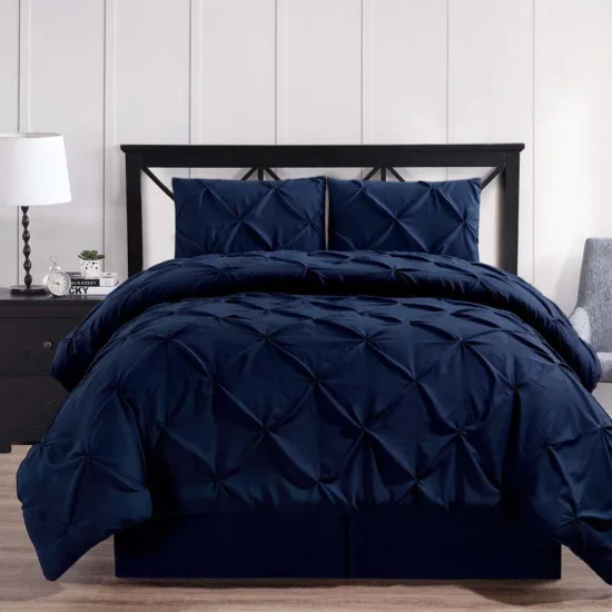 A navy pinch pleated comforter set with two matching shams on a black metal bed frame beside a white lamp