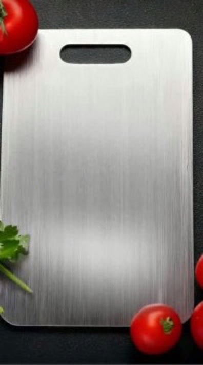 Seller's photo of the Katori board lying on a dark slate counter, brushed metal face, with cherry tomatoes and a sprig of cilantro beside it