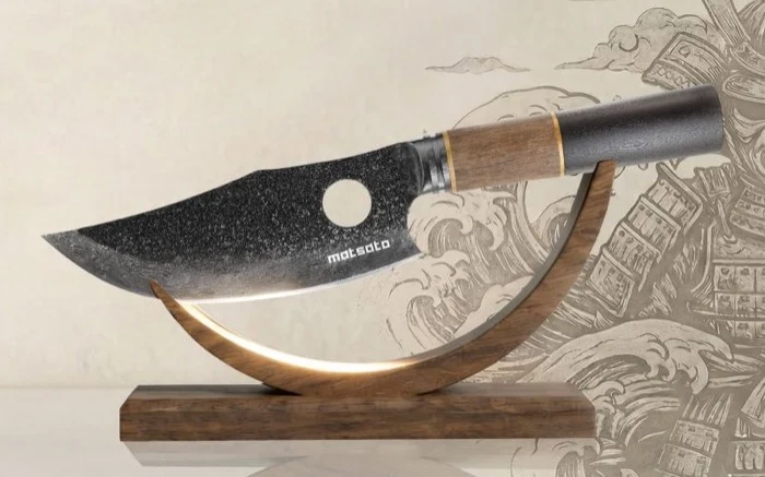 The Matsato Osuren knife on its curved wooden stand, the blade's dark stonewashed finish, the finger hole and the wood-and-dark-handle grip visible