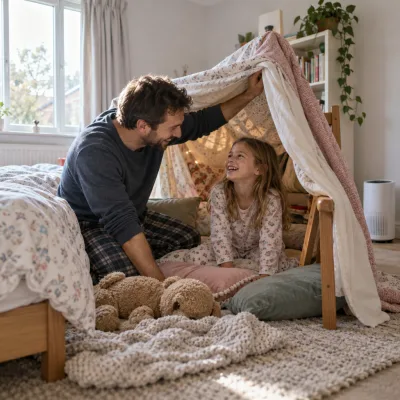 A father and his young daughter laugh as they build a blanket fort in a bright bedroom
