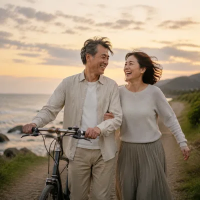 A couple in their fifties walking a bicycle along a coastal path at sunset