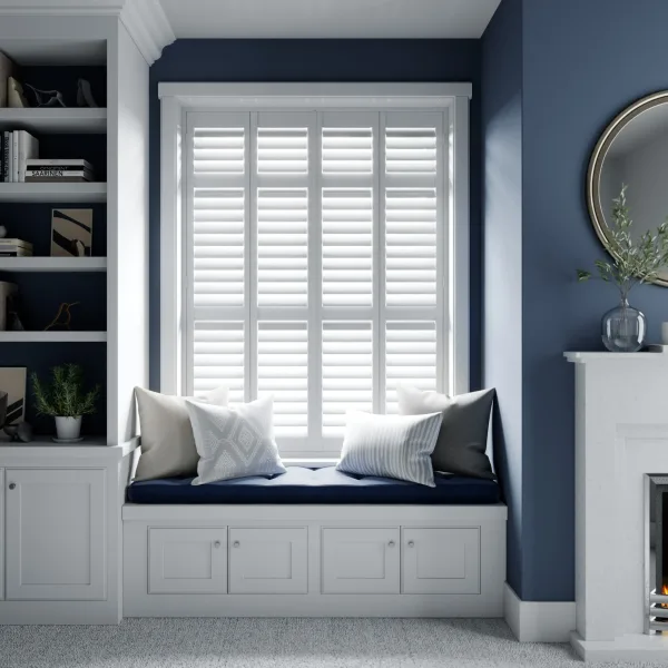A white hardwood shutter filling a window above a built-in window seat with navy and white cushions, between navy walls and a white fireplace