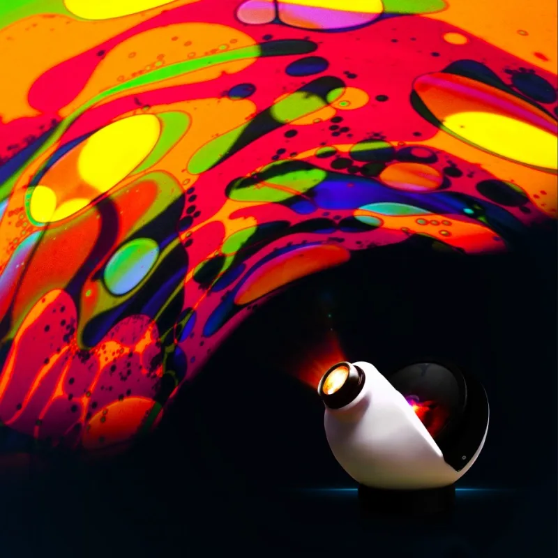 A white OPTI Aura sensory projector on a round black base throwing a liquid effect of orange, red, green and blue blobs across a dark wall